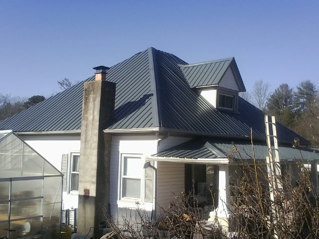 Dark blue standing seam metal roof on a white farmhouse with dormer — Slate & Tile Roof Repair by Roofing Brothers in Bliss