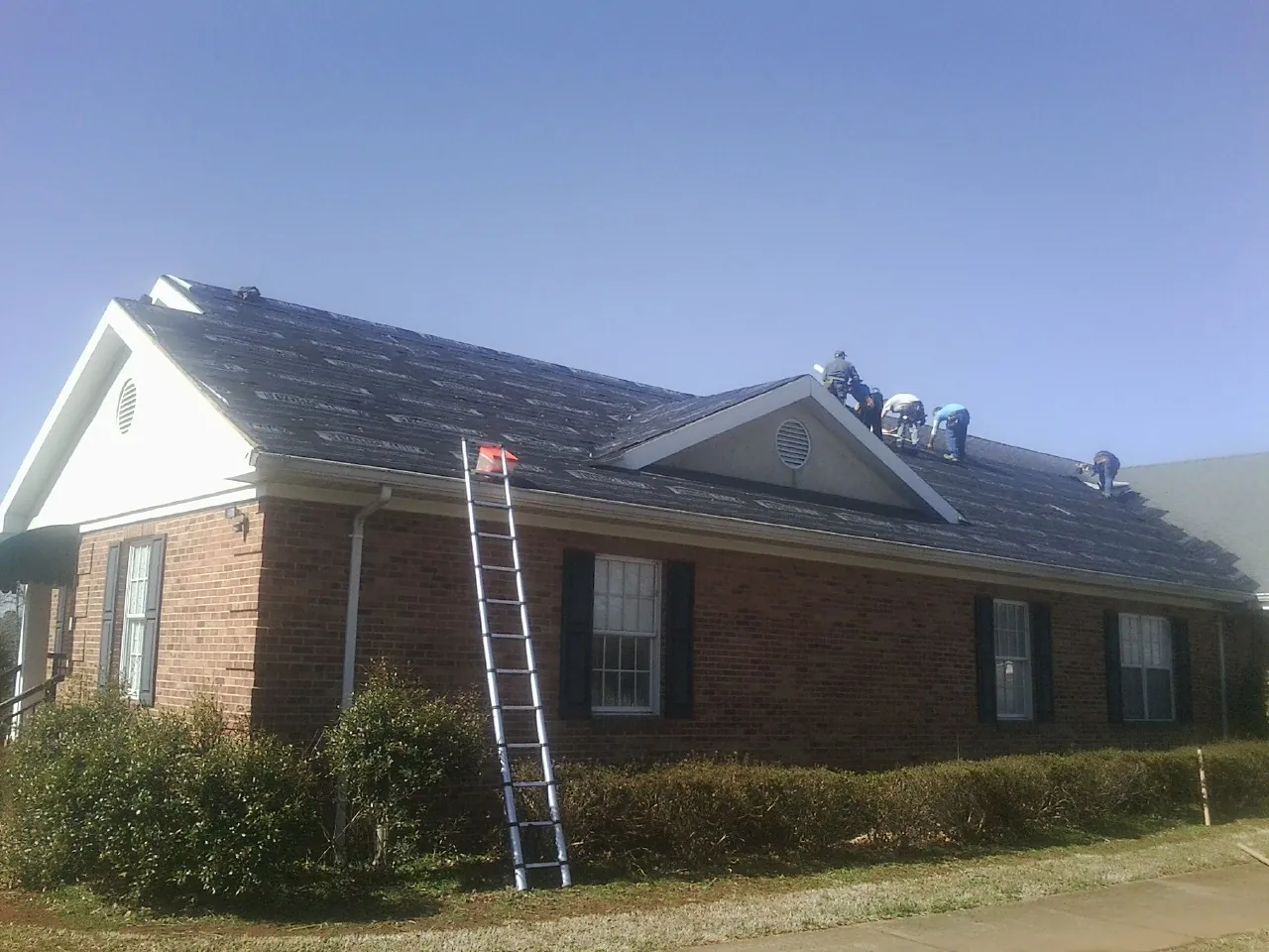 Crew tearing shingles off a brick ranch roof with a ladder set — Emergency Roof Repair work by our crew in Bliss