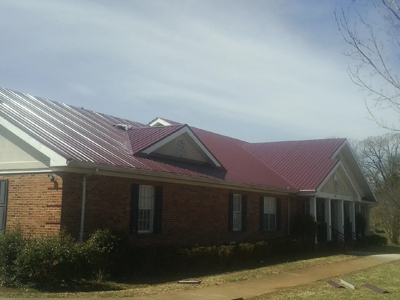 Red metal roof with gabled entries on a long brick building, from a Hail Damage Roof Repair job in Bliss