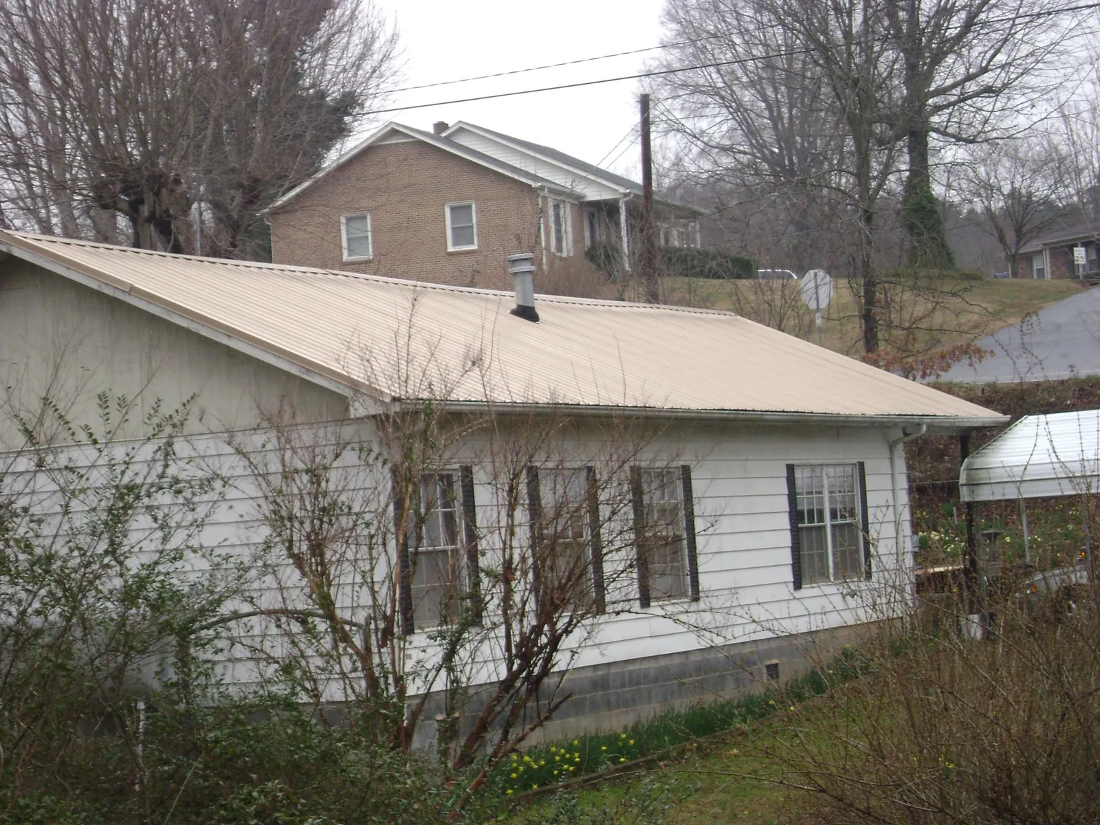 Tan metal roof on a white sided house set into a hillside — Commercial Roofing by Roofing Brothers in Bliss